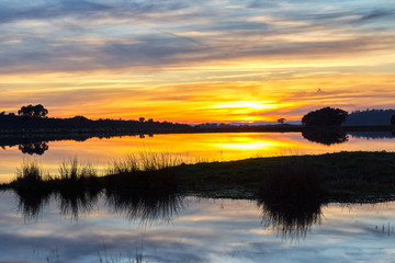 landscape at sunset with reflection of the sky over the water of a lake.