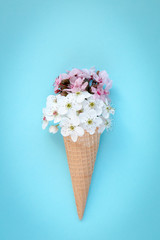 Fashion food set of Ice cream cone with white and pink flowers on top over a blue background, minimalistic design.