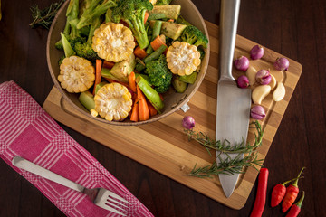Roast vegetables, herbs and spices on chopping board with knife, food and cooking stock lay flat image.