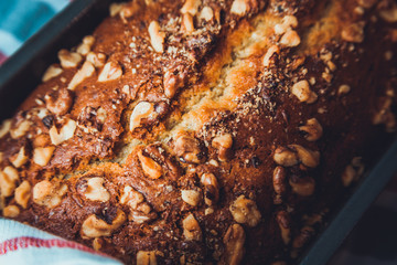 Freshly Baked Banana Bread With Walnuts In A Baking Pan On A Red, White and Gray Kitchen Towel