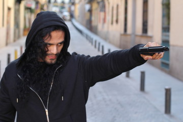 Hooded ethnic criminal holding a gun outdoors