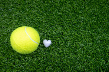 Tennis ball with white heart shape on green grass