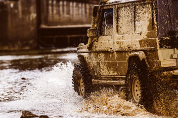 Mud and water splash in off the road racing. Bottom view to big offroad car wheel on country road and mountains backdrop. Off-road vehicle goes on the mountain.