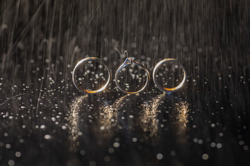 Wedding rings lying on dark surface shining with light close up macro. Water splashes. Rain