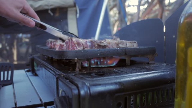 Man moving lamb chops around a hot plate. Gas fired stove top cooking meat with man using tongs. LOW ANGLE