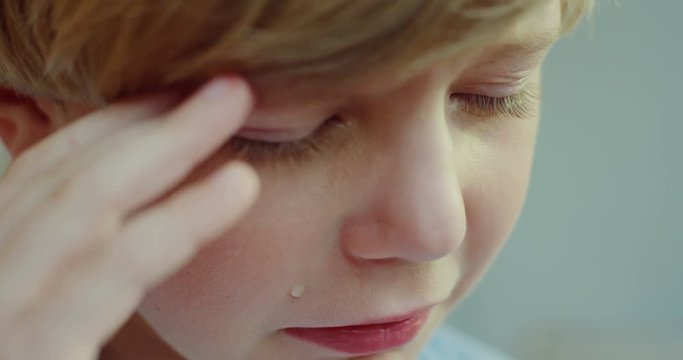 Close up of the sad small blonde Caucasian boy crying and having hysterics, then wiping eyes with hands.
