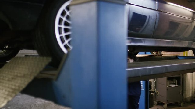Car mechanic inspecting under carriage of a car on a raised ramp