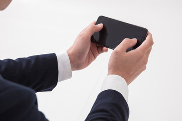 白背景で上半身でスーツの男性がスマートフォンを休憩中にゲームをしている場面