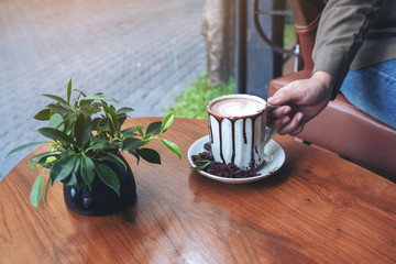 Closeup image of a hand holding a cup of hot chocolate on wooden table in cafe