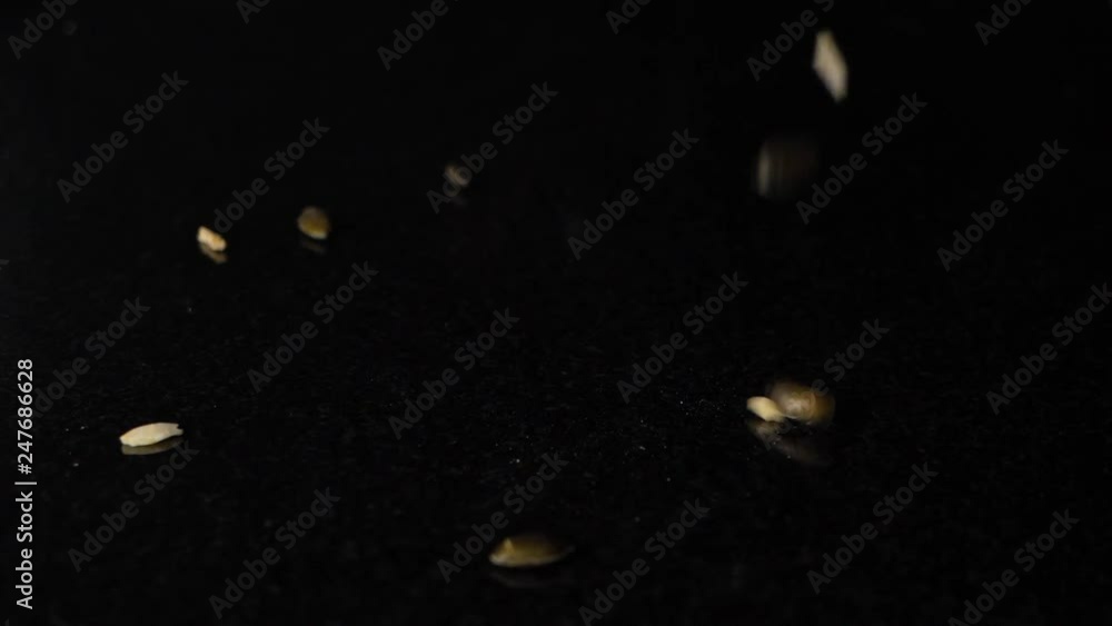 Poster kernel dropping in slow motion on a black surface, isolated in black background.