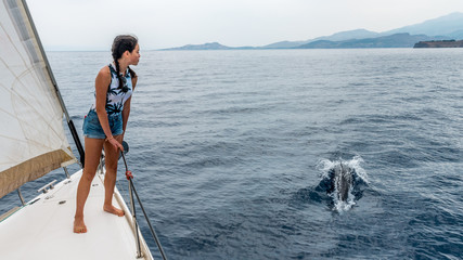 young teen standing on the deck of a sailboat with dolphin © David