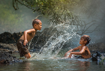 Asia children on river / The boy friend happy funny playing water in the water stream in countryside