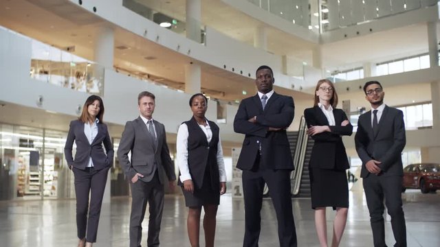 Group of six confident businesspeople of different ethnicities posing for camera in business center