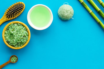 Asian spa treatment concept with natural ingredients. Spa salt, lotion, sponge near bamboo on blue background top view space for text