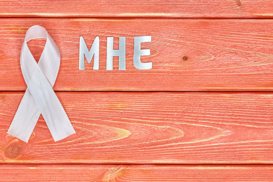 white awareness ribbon and inscription of iron letters: mhe, lying on wooden textured background color of season 2019