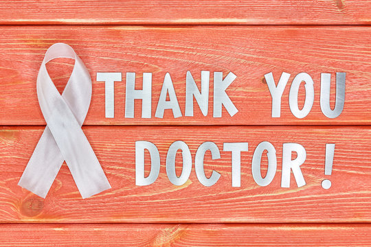 white awareness ribbon and inscription of iron letters: thank you doctor lying on wooden textured background color of season 2019