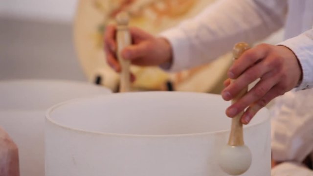 Man playing crystal bowls and singing. Close up on man's hands playing crystal bowls and singing with various sacred objects displayed around him, side view
