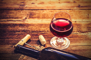a glass of red wine, a bottle and a bunch of grapes on an old wooden kitchen table.