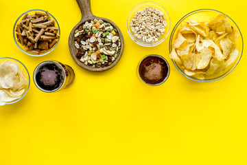 Fast food for TV watching. Snacks on desk.  Chips, nuts, rusks and beer on yellow background top view space for text