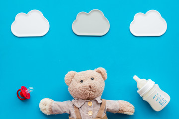 Feed baby concept. Teddy bear toy near small bottle with food on blue background top view copy space