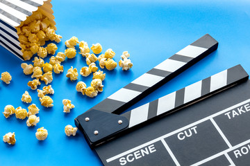 Film watching concept. Clapperboard and popcorn on blue background copy space