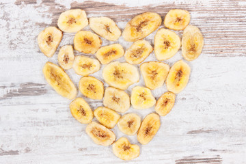 Dried organic banana chips in shape of heart on rustic board