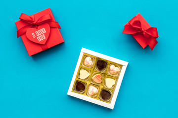 Gift for Valentine's day. Gift box with text I love you and heart-shaped sweets on blue background top view copy space