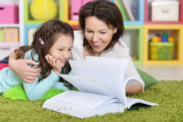 mother with  daughter reading book while lying on floor