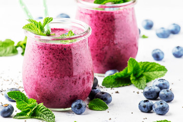 Purple homemade yogurt or smoothie with blueberries, chia seeds and mint leaves in glass jars on...
