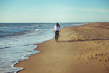 Woman rides a Bicycle along the sea on a sandy beach. Back view.