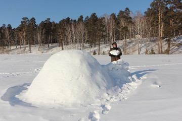 Man in warm clothes building an igloo on a snowy glade in the winter, Siberia, Russia