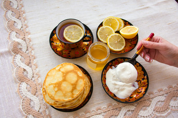 tea in a painted Cup, on a saucer sliced lemon, pancakes, sour cream and a wooden spoon for overlaying. tea party in rustic style