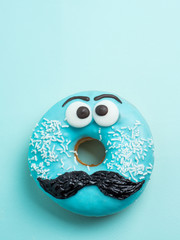 Blue glazed donut with mustache. Blue doughnut with funny face with mustache on blue background....