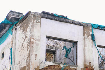Destroyed building, housing in disrepair, demolition of the old house on grey sky background.