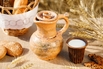 bread , cookies and milk in ceramic jug, wheat ears on the rustic bagging table, wheat field. Healthy breakfast