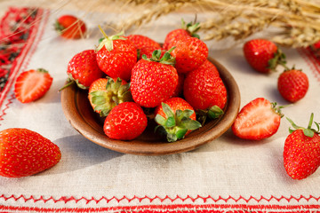 Ceramic bowl with strawberries on rustic background with wheat ears. Close up, high resolution product. Harvest Concept