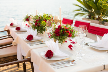 table for a wedding dinner decorated with red flowers and greenery