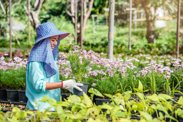 Happy worker asian woman with planting flowers taking care of flowers in greenhouse.