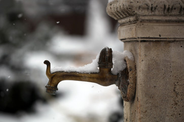 Old copper tap in winter in the garden, covered with fresh soft snow. Winter blurred background.