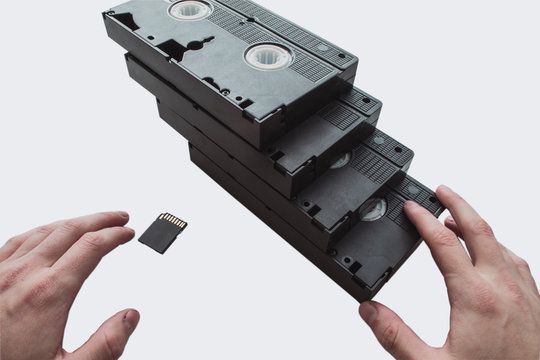  Several old videotapes are on a white background, one on the other and one flash drive. Old and modern way to save information. Flash card and videotapes in  human hand.