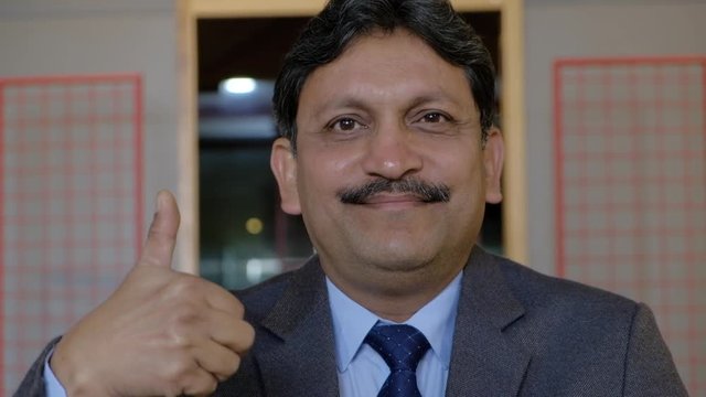Shift focus to an Indian man tasing his hand and sign best of luck with his hand raised in sign and then the camera tilts down to his hands of the table