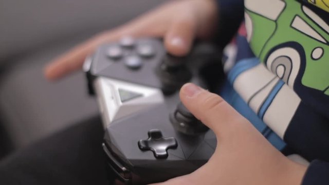 Small boy hands holding wireless gamepad and playing video games in a livingroom