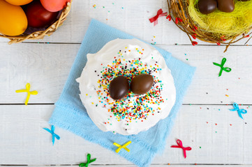 Traditional Easter cake - kulich and chocolate eggs in a nest on a wooden white background. Sweet bread decorated meringue. Top view. Easter theme.