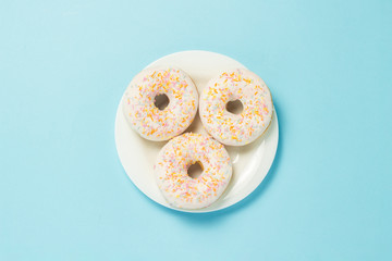 Donuts on a white plate on a blue background. The concept of fast food, morning coffee, breakfast. Minimalism. Flat lay, top view.