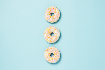 Three fresh delicious sweet donuts laid out in a row on a blue background. Fast food concept, bakery, breakfast,. Minimalism. Flat lay, top view.