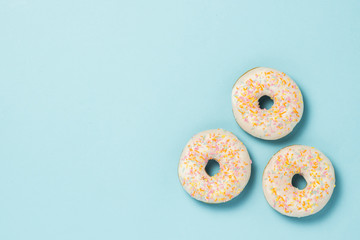 Three fresh delicious sweet donuts on a blue background. Fast food concept, bakery, breakfast,. Minimalism. Flat lay, top view.