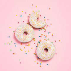 Fresh tasty sweet donuts, multicolored decorative candies, sugar cubes on a pink background. Bakery concept, fresh pastries, delicious breakfast, fast food. Flat lay, top view.