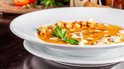 The concept of Italian cuisine. Pumpkin cream soup with orange flavor, chicken pieces, bread croutons and cream. A string of red wine on the table. Serving dishes in the restaurant