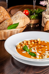 The concept of Italian cuisine. Pumpkin cream soup with orange flavor, chicken pieces, bread croutons and cream. A string of red wine on the table. Serving dishes in the restaurant