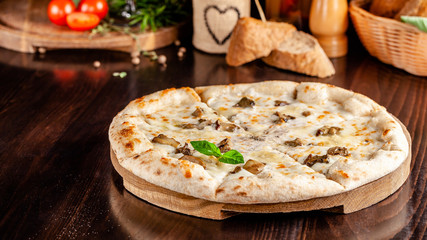The concept of Italian cuisine. Thin cheese pizza with mushrooms, with large sides of Semola flour. A string of red wine on the table. Serving dishes in the restaurant